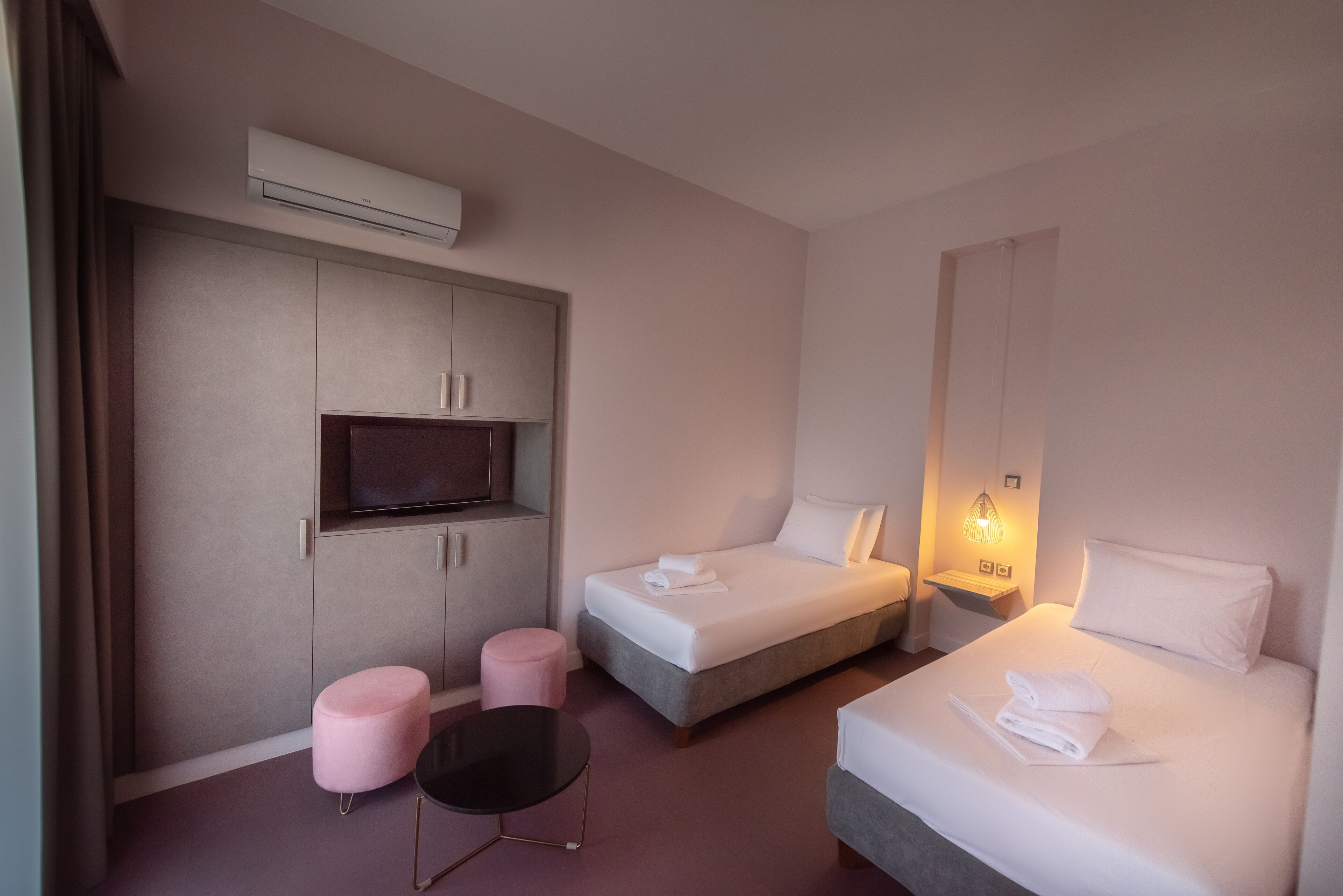Una habitación de hotel moderna con dos camas, un televisor, una mesita pequeña y un otoman rosa.