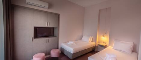 A modern hotel room with two beds, a TV, a small table, and a pink ottoman.