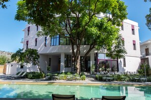 Un bâtiment moderne doté d’une piscine, d’un espace extérieur aménagé et d’un grand arbre à l’avant.