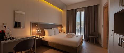 Een hotelkamer met een bed, bureau, stoel en een groot raam met gordijnen.