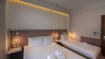 Ein Hotelzimmer mit zwei Betten, einem Nachttisch, einer Lampe und ordentlich gefalteten Handtüchern.