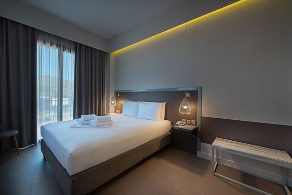 Une chambre d’hôtel moderne avec un grand lit, des lampes de chevet, une table de nuit et une vue sur la ville par la fenêtre.