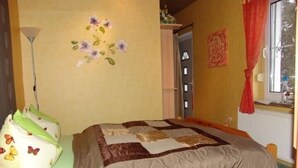 Une chambre à coucher avec un lit en bois, une décoration murale à motifs floraux, une fenêtre avec un rideau rouge et un radiateur.