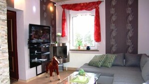 Un salon avec un canapé, une table basse en verre, un téléviseur et un rideau rouge.