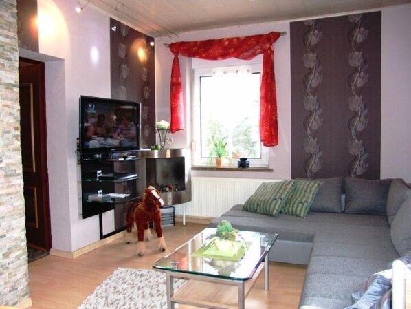 A living room with a sofa, a glass coffee table, a TV, and a red curtain.