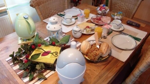 Une table à manger dressée avec des assiettes, des bols, un pichet et une tasse, entourée de chaises en osier.