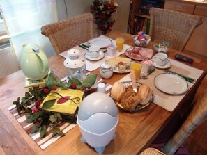 Mesa de jantar posta com pratos, tigelas, jarra e xícara, rodeada por cadeiras de vime.