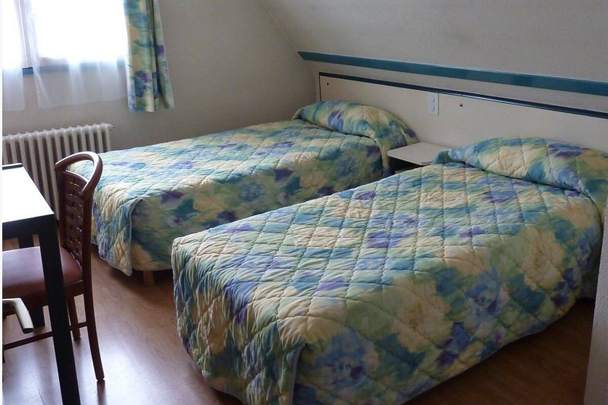 A room with two single beds, a wooden chair, and a table.