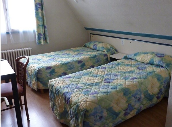 Una habitación con dos camas individuales, una silla de madera y una mesa.