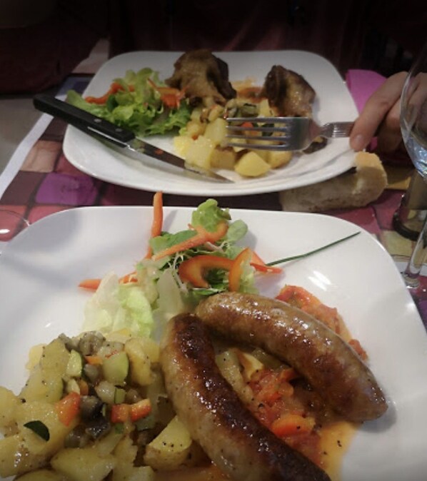 Una mesa de comedor con platos de comida, incluyendo salchichas, papas y verduras.