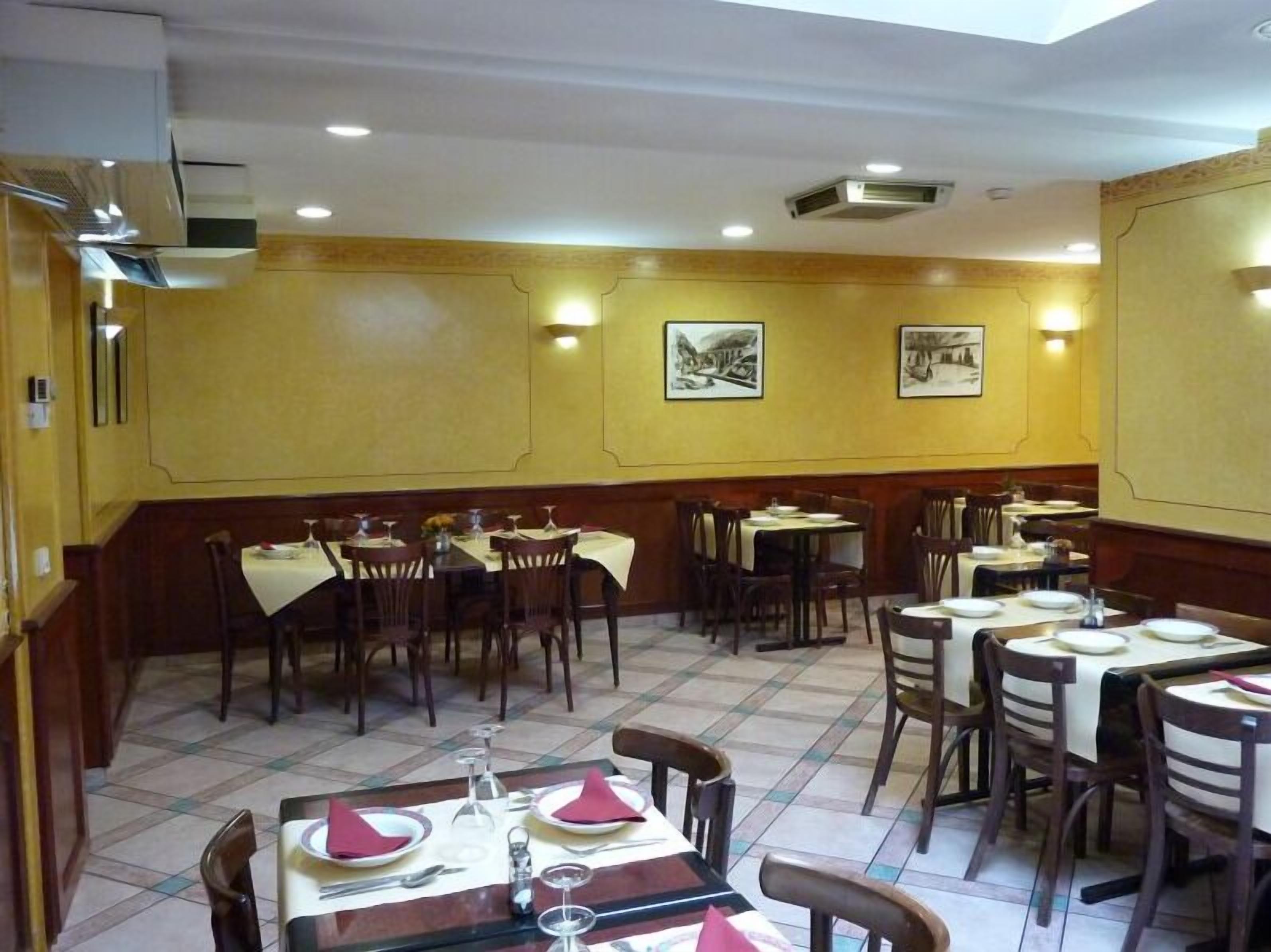 Un interior de restaurante con mesas y sillas de madera, piso de baldosas y luces fijadas a la pared.