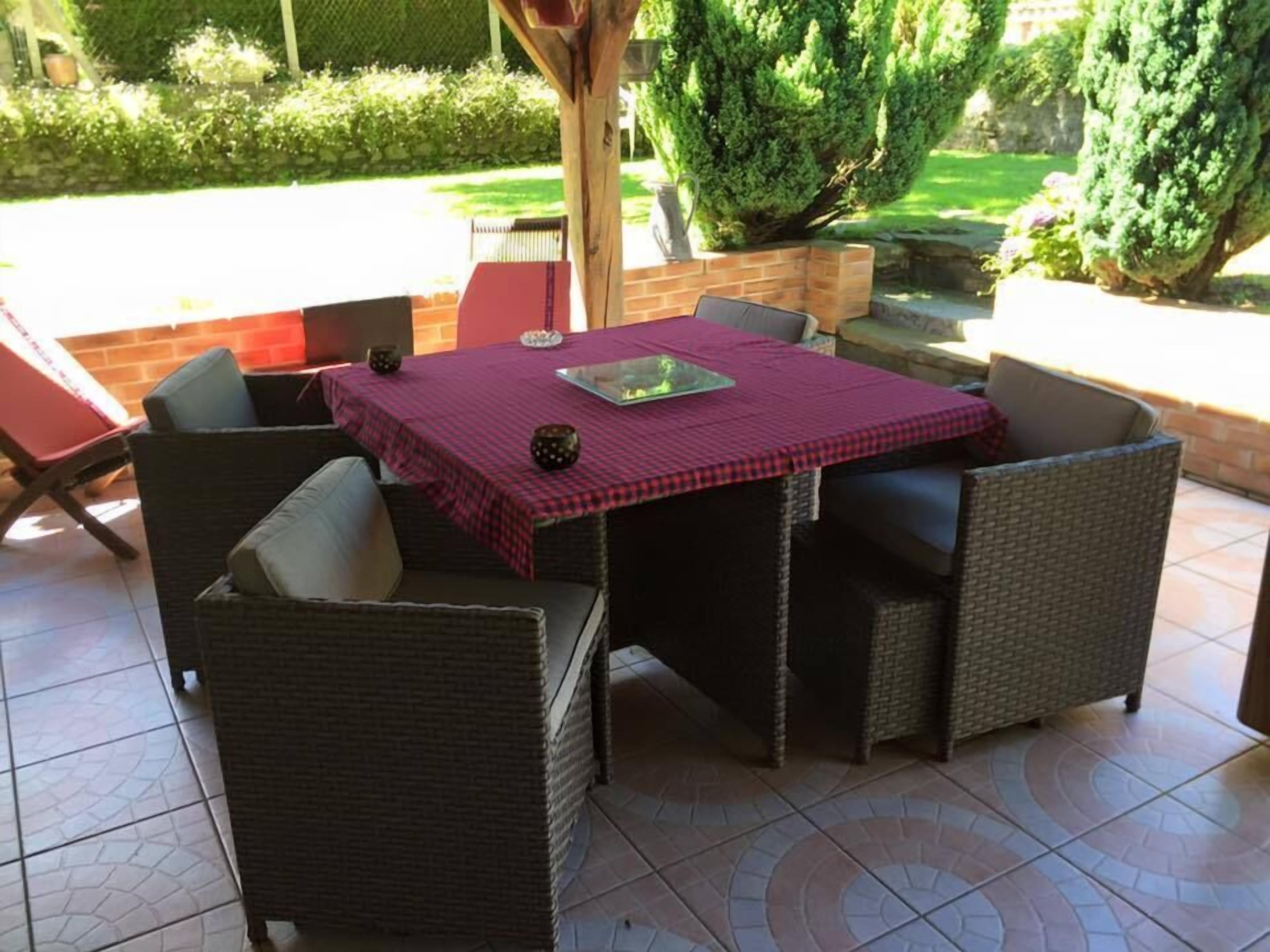 Een terras buiten met een tafel voor vier personen, omringd door rieten stoelen.