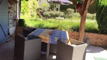 Een terras buiten met rieten meubels en een tafel bedekt met een tafelkleed met een patroon.