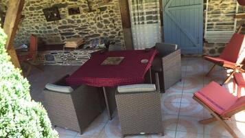 An outdoor patio with stone walls, wicker furniture, and a tiled floor.