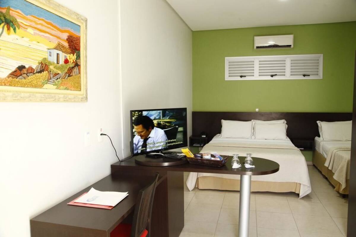 Ein Hotelzimmer mit einem Bett, einem Schreibtisch mit Computer, einem Fernseher und einem Bild an der Wand.