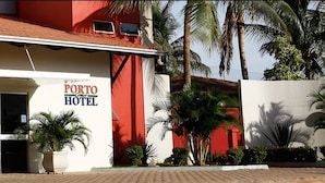 A hotel named "Porto Hotel" with a red facade, large windows, and palm trees in the foreground. - Porto Center Hotel (Luís Eduardo Magalhães)