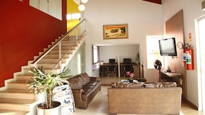 A spacious living area with a staircase, a sofa, a coffee table, and a television. - Porto Center Hotel (Luís Eduardo Magalhães)