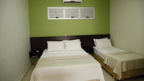 A hotel room with two beds, a nightstand, a wall-mounted air conditioner, and a window with shutters. - Porto Center Hotel (Luís Eduardo Magalhães)