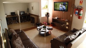 A living room with a brown leather sofa, a coffee table, a TV, a fireplace, and a dining area with a desk and chairs. - Porto Center Hotel (Luís Eduardo Magalhães)