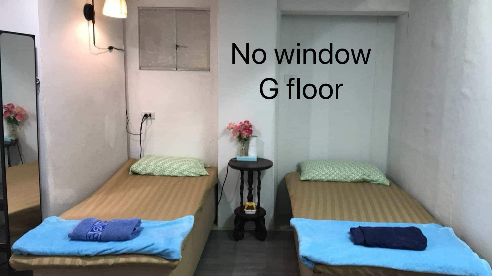 Un petit logement composé d’une seule pièce, comprenant deux lits, une petite table et un luminaire fixé au mur.