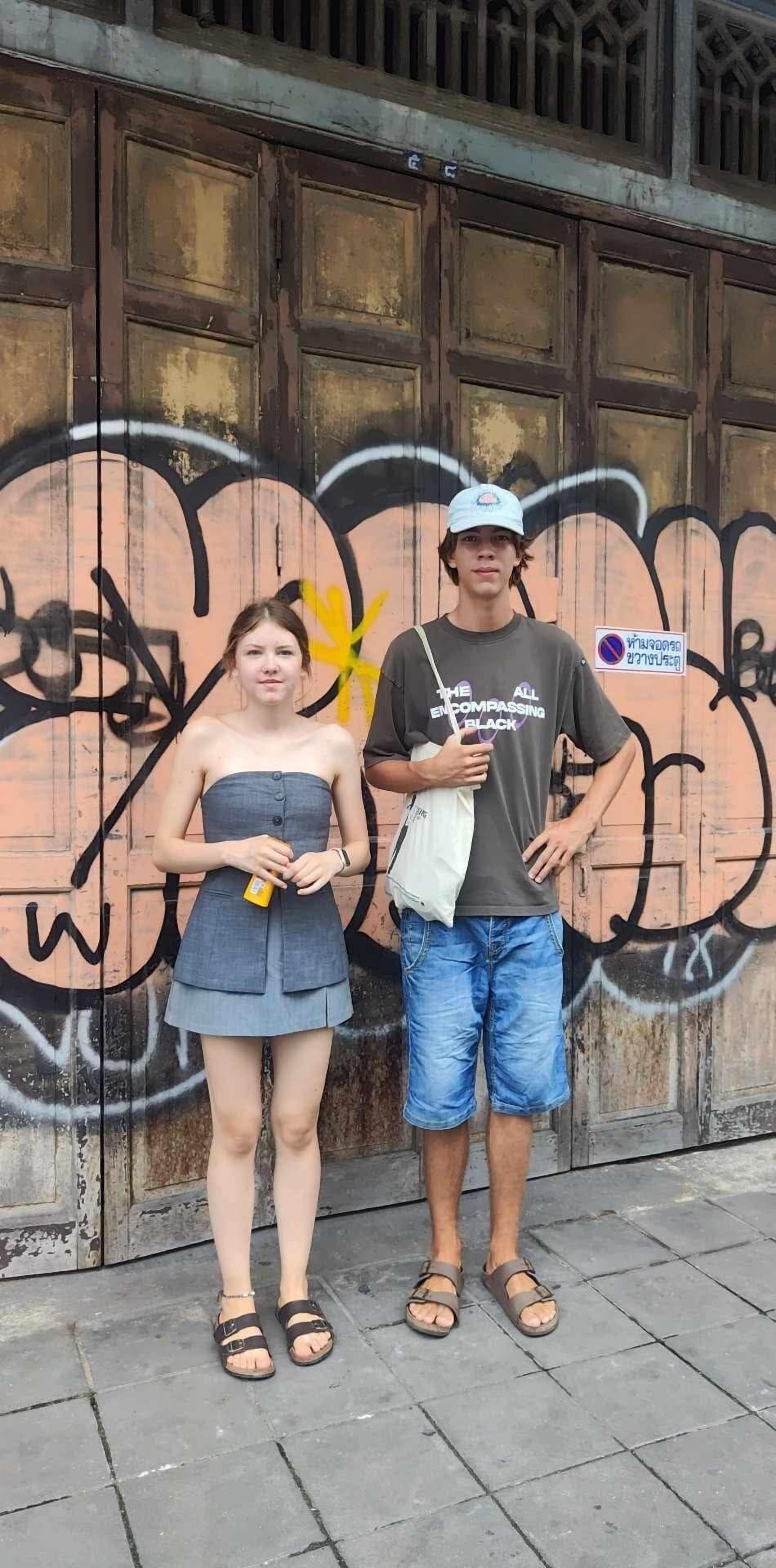 Ein Mann und eine Frau stehen vor einer Holztür mit Graffiti.