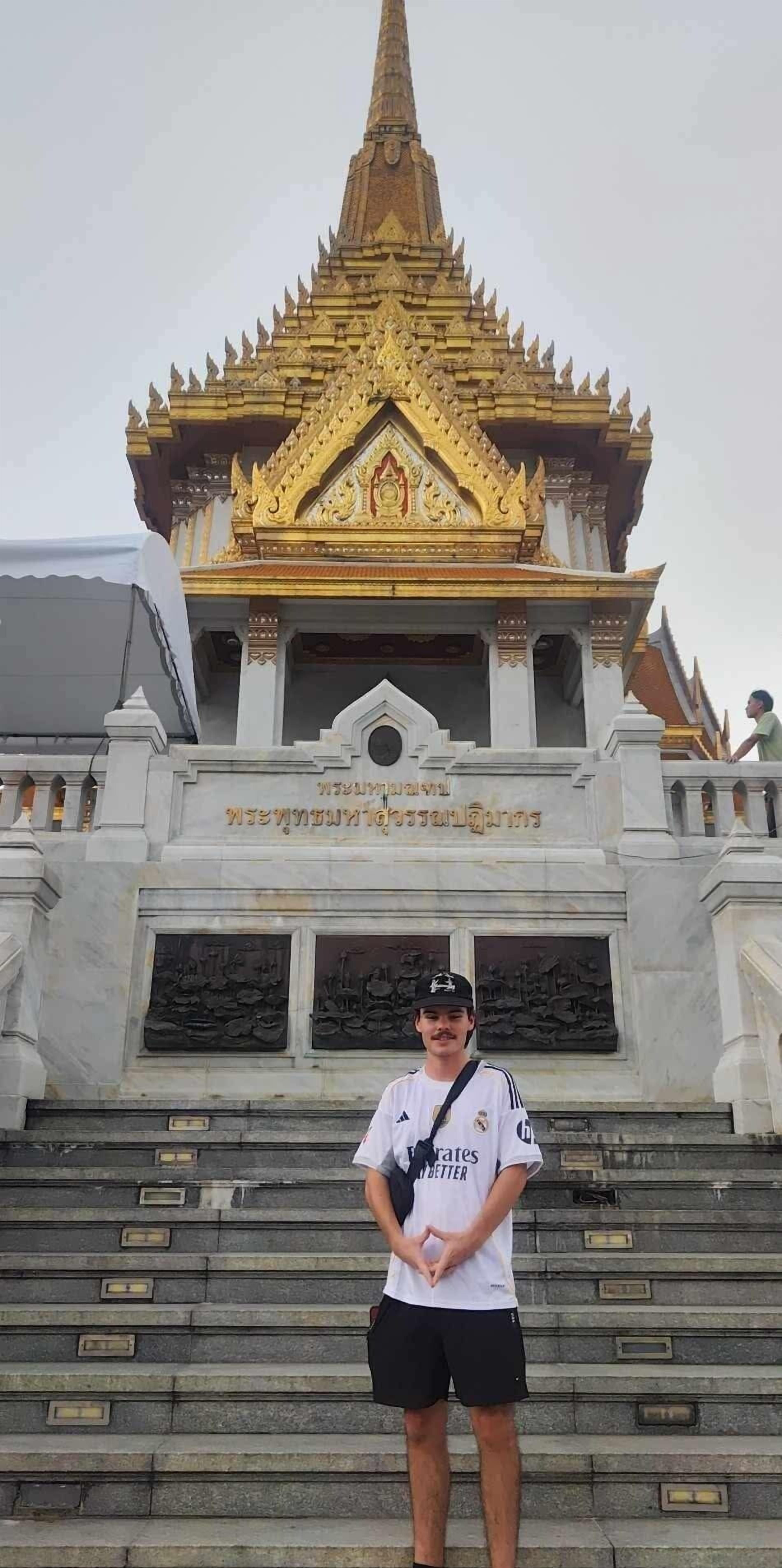 A person standing in front of a temple with a golden spire and inscriptions.