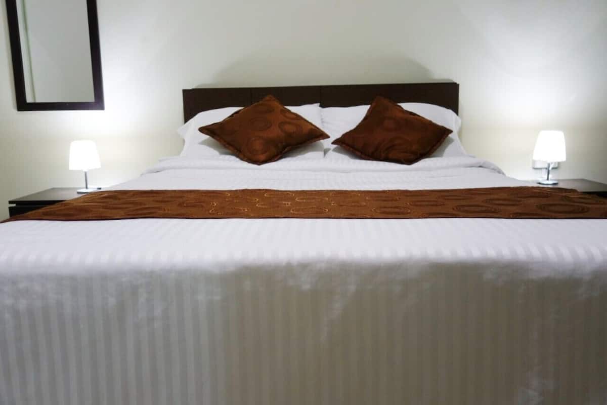 A neatly made bed with a brown patterned bedspread and two brown pillows. There are two bedside lamps on either side of the bed.