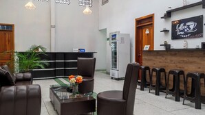 Um hall com sofás de couro, um balcão de recepção, um aviso de café e uma geladeira.