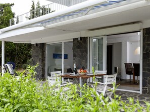 Uma área de estar moderna ao ar livre com uma mesa e cadeiras, rodeada por vegetação.