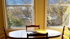 Un coin repas avec une table ronde et quatre chaises, de grandes fenêtres équipées de stores et une vue sur les montagnes.