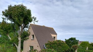 A single-story house with a sloped roof, surrounded by lush greenery and flowering bushes. - Villa Oostduinkerke, 400m sea+dunes,quiet+green+much light, 6p+baby,3bed+2bath (Koksijde)