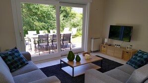 A modern living room with grey sofas, a coffee table with decorative items, a TV, and a sliding glass door leading to an outdoor patio. - Villa Oostduinkerke, 400m sea+dunes,quiet+green+much light, 6p+baby,3bed+2bath (Koksijde)