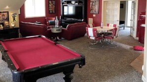 Una mesa de billar, un televisor, una mesa de comedor con sillas y un sofá rojo en una habitación con alfombra.