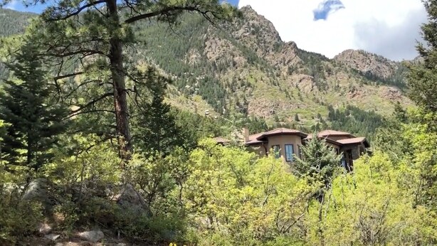 Una cabaña de montaña con dos edificios, rodeada de un bosque denso y montañas rocosas.