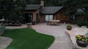 Un patio con piso de piedra, césped, una cabaña de madera y mobiliario exterior.