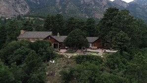 Una cabaña con un patio, rodeada de un bosque denso y montañas.