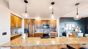 A modern kitchen with granite countertops, wooden cabinets, and pendant lighting.