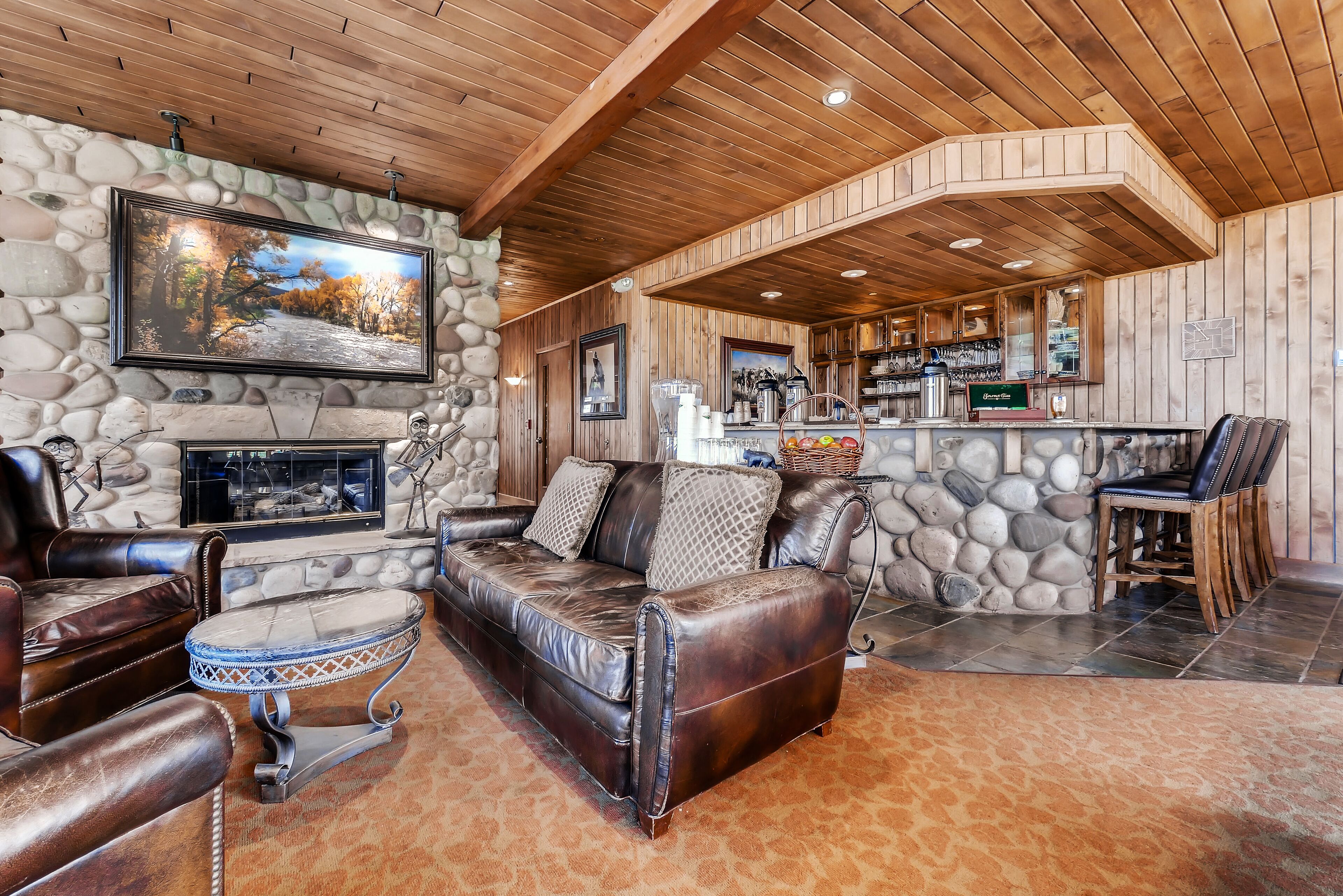 A cozy living room with a stone fireplace, leather sofa, and a bar area with a stone wall.
