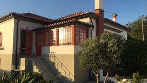 A two-story building with a red door, multiple windows with red frames, and a chimney.