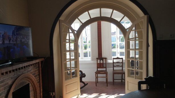 A room with a fireplace, a television, and a large arched doorway leading to an outdoor area with chairs and a table.
