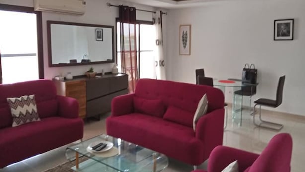 A living room with red sofas, a glass coffee table, and a dining area with a glass table and chairs.