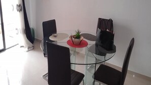 A modern dining area with a glass table, black chairs, a red placemat, and a small potted plant.