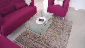A living room with a glass coffee table, two pink sofas, and a grey shaggy rug.