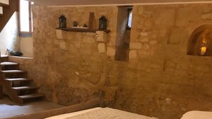 Ein Schlafzimmer mit Steinwand, einem Bett mit Decke, einem Nachttisch mit Lampe und einem Fenster mit Blick auf eine Treppe.