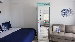 Ein Schlafzimmer mit einem Bett, einem grauen Sofa und einem Flur, der in einen Wohnbereich führt.