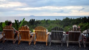 Vier Holzsessel, die auf einen weiten Blick über das Meer mit einer entfernten Insel zeigen.