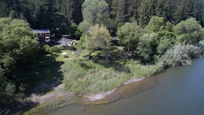 An aerial view of a lakeside property with a house, a deck, and a grassy area with trees. - River View Garden Resort (Monte Rio)