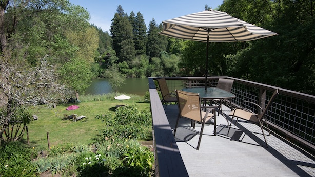 A deck with a table and chairs, overlooking a lake and surrounded by trees. - River View Garden Resort (Monte Rio)