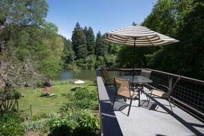 A deck with a table and chairs, overlooking a lake and surrounded by trees. - River View Garden Resort (Monte Rio)