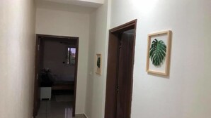 A hallway with a bed in the background, a door on the right, and a framed plant on the wall. - Résidence italien2  T3 (Abidjan)